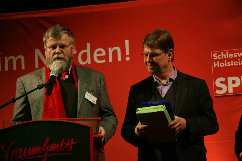 two men are standing at podiums speaking