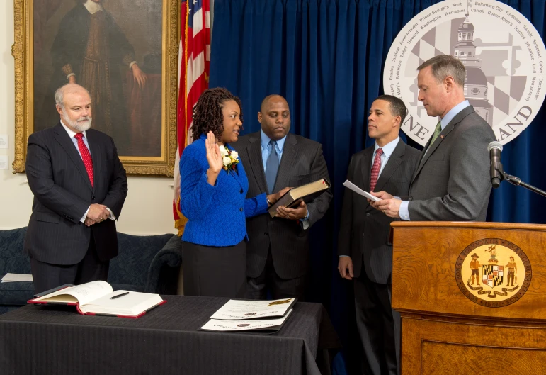 a woman speaking at a podium while some other people look on