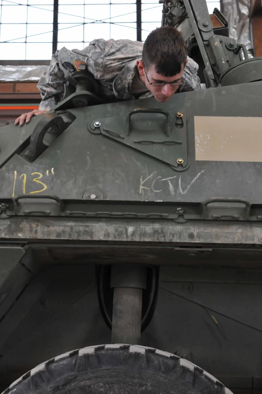 man in uniform climbing on top of the military vehicle