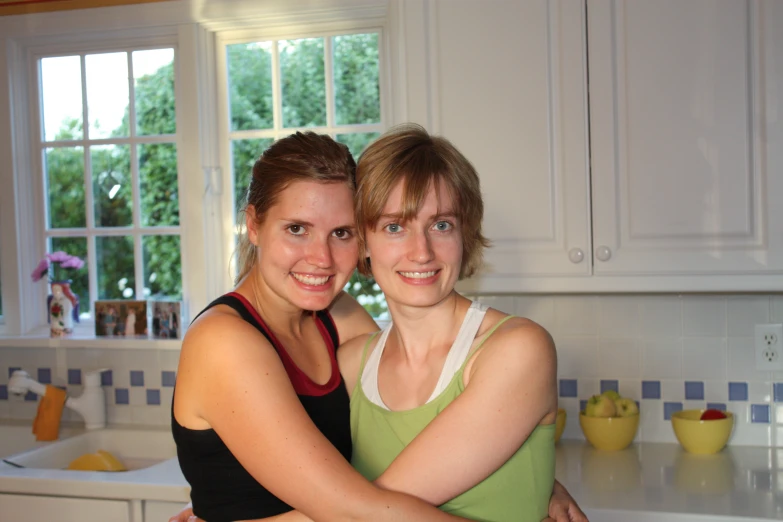 two girls, one in a green tank top and one in blue tank top, standing in a kitchen