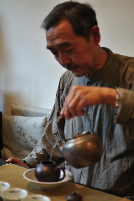 a man sitting down pouring some liquid from a teapot