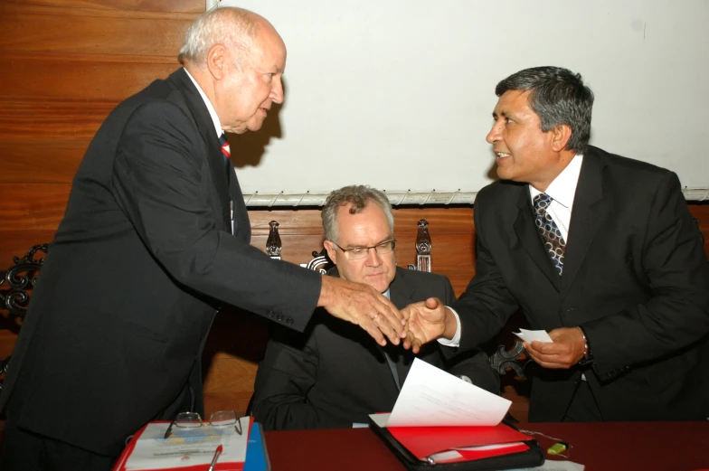 two men are shaking hands as one looks on