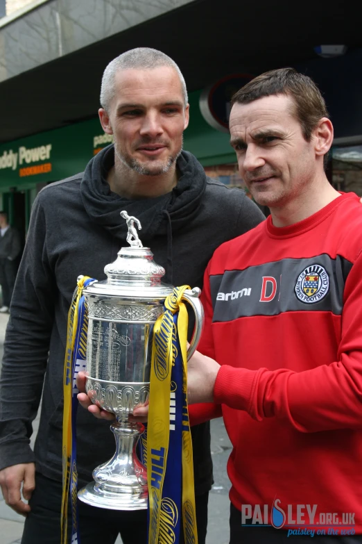 two men standing next to each other holding onto a trophy