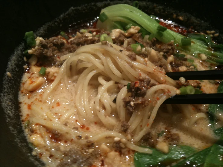 a bowl of noodles, meat and broccoli are being stirred