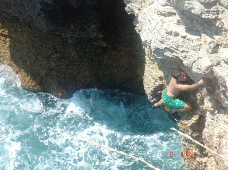 the man is climbing up the cliff on the water