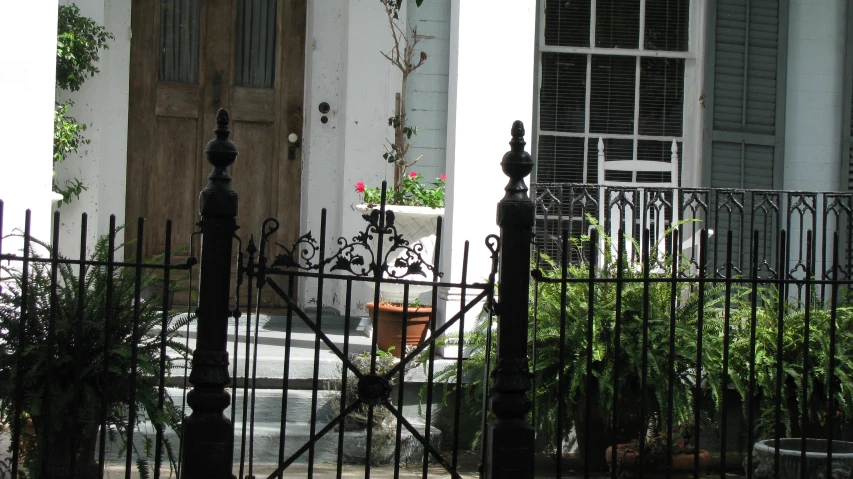 the view of a white house from the street with black wrought iron fence and door