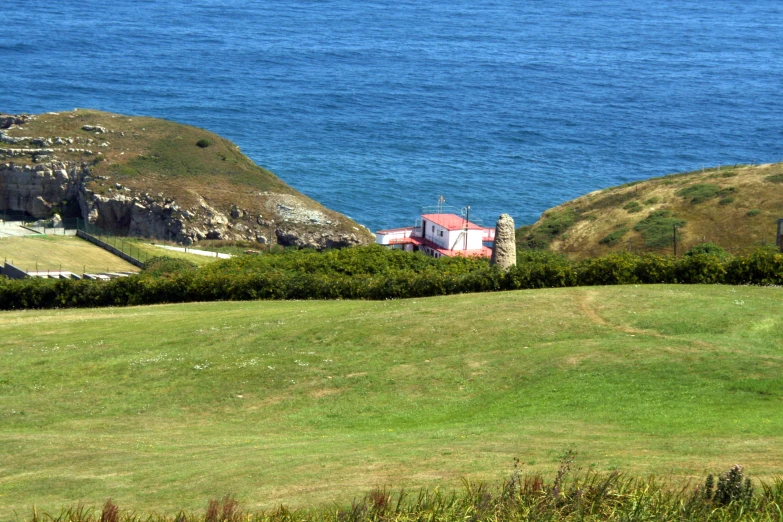 a house in the middle of a grassy field next to the ocean