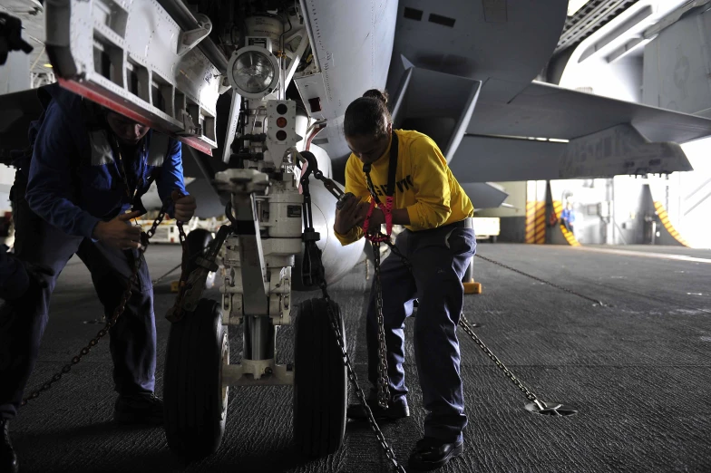 two pilots are using chains to work on the tire of an aircraft