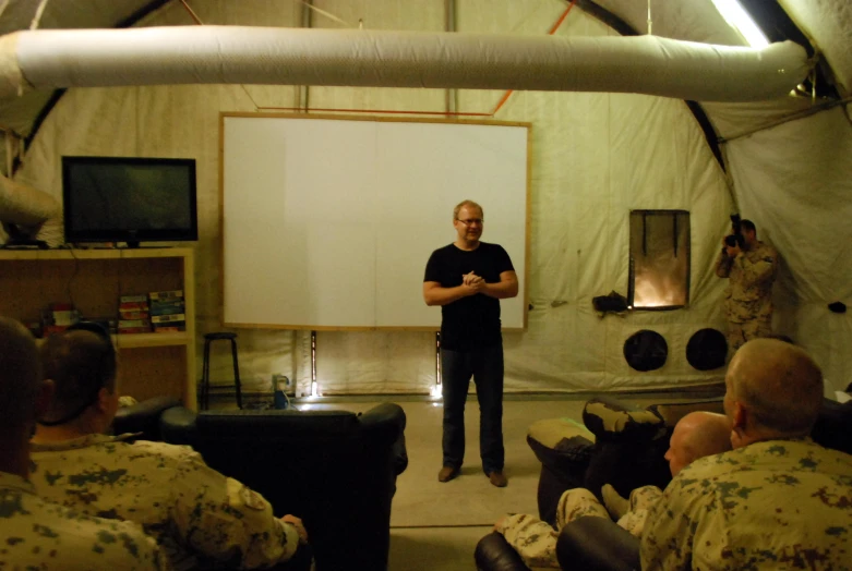 a man in black shirt and military pants standing in front of a presentation