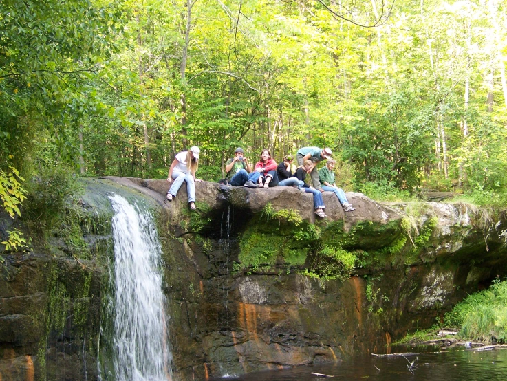 some people are sitting on a rock by a waterfall