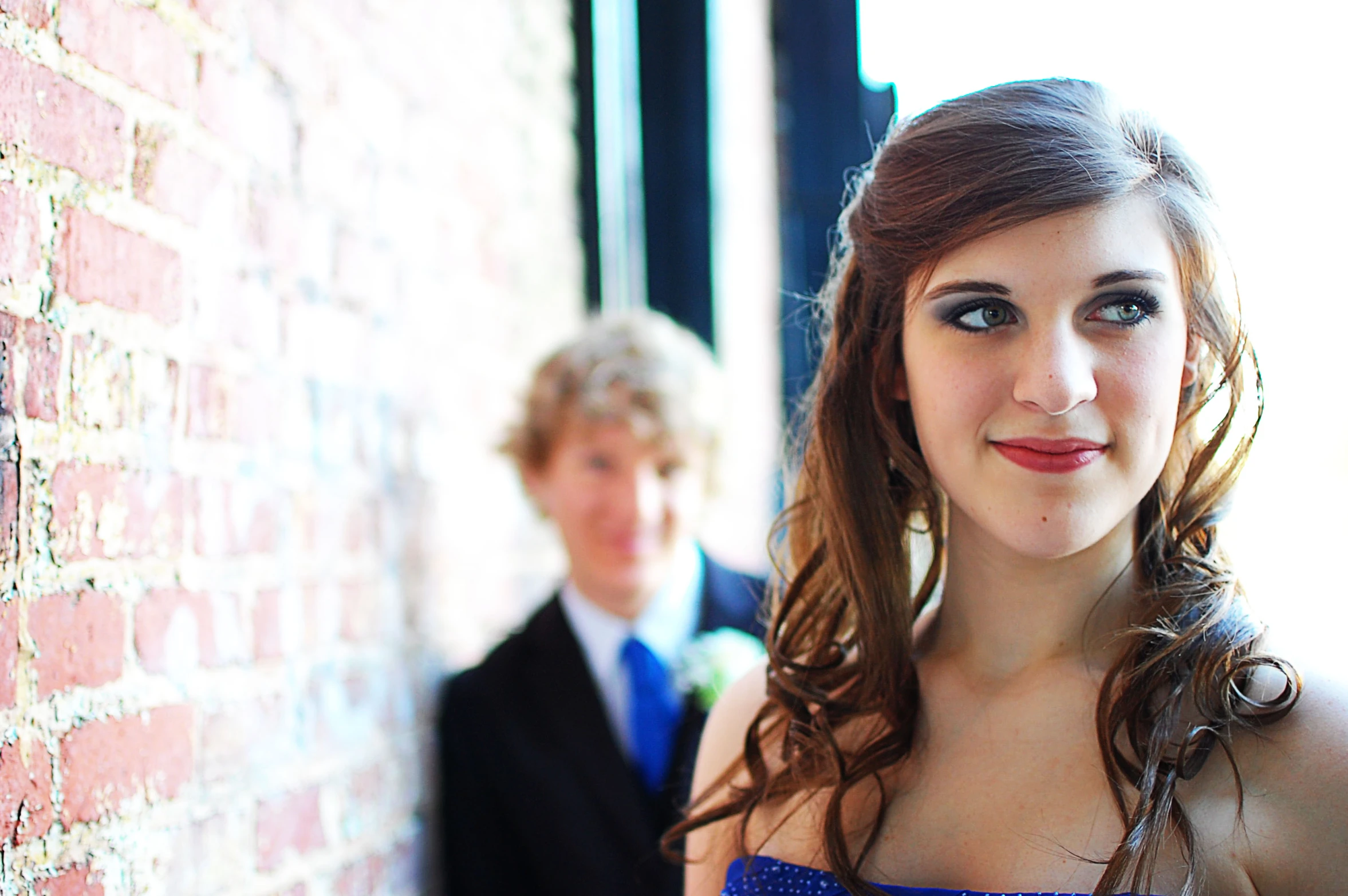 a young woman in a blue dress leaning against a brick wall