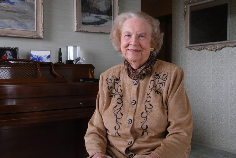 an older woman sitting next to a wooden piano