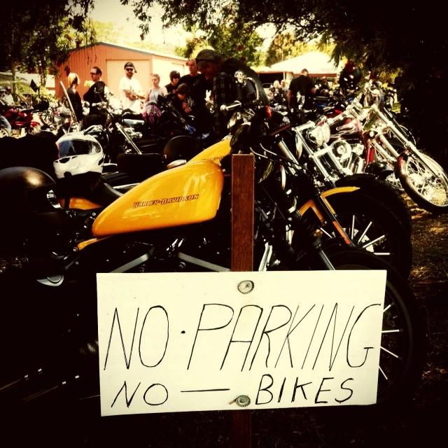 a sign with some motorbikes on the grass and buildings