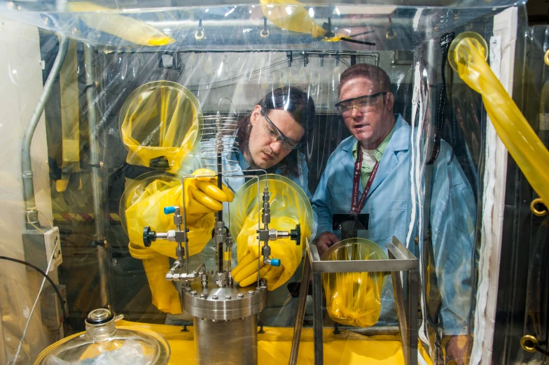 two men in yellow suits with tools inside a machine