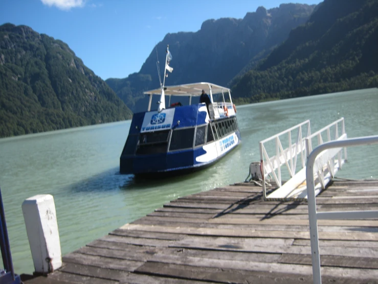 a blue and white ferry sitting on the side of a lake