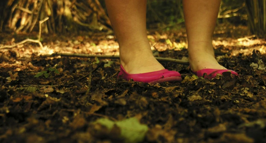 a woman's feet with pink shoes on standing in leaves