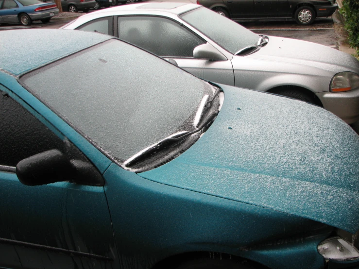 two parked cars in a parking lot with snow on the windscreen