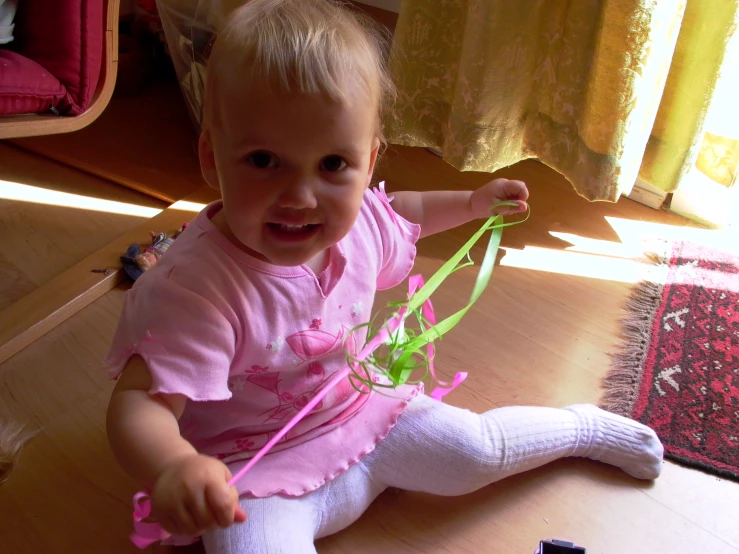 an infant sitting on the floor with a string in her hand