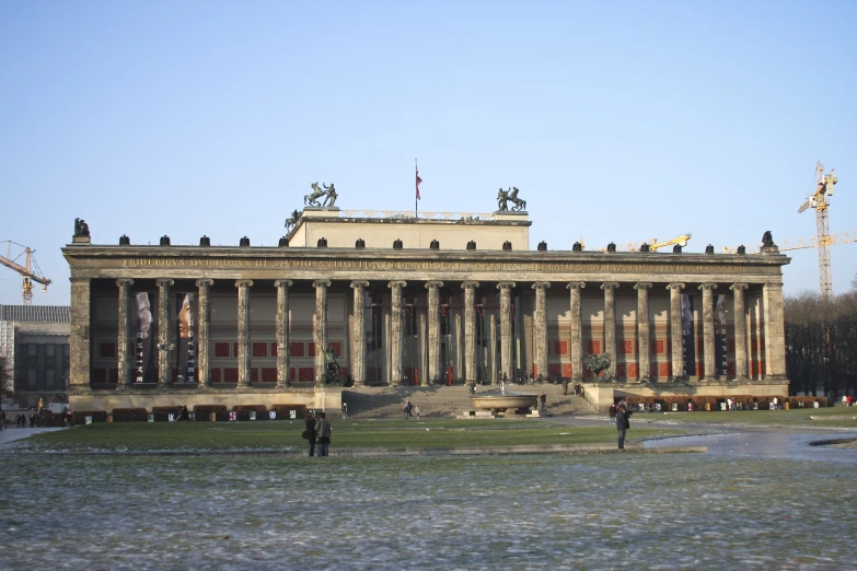 people walking and sitting in a grassy area in front of a building