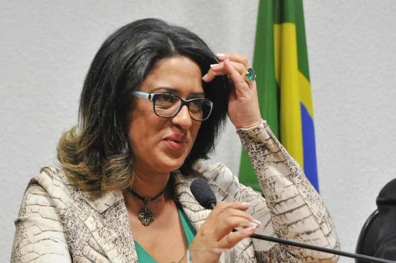 woman with glasses speaking in front of a flag