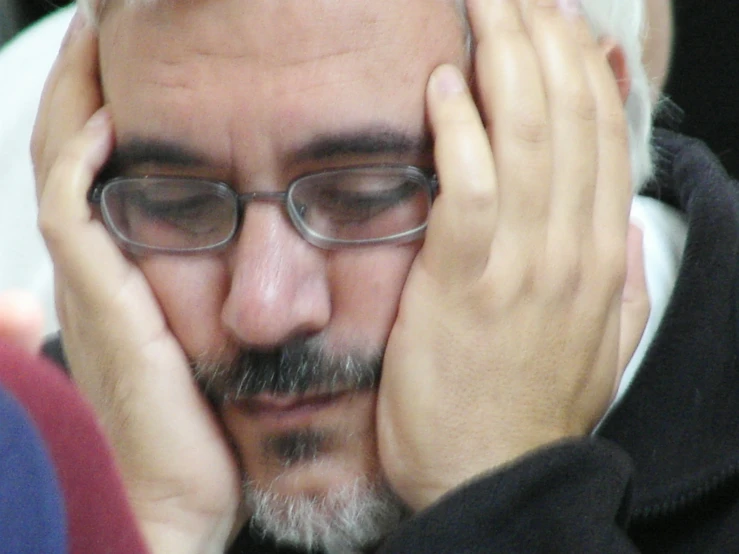 an older man with glasses is putting his head in his hands