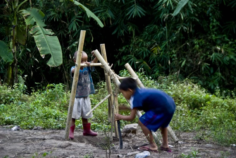 two children trying to build a wooden structure in a forest