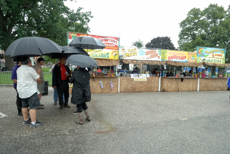 three people standing under a black umbrella near a stand of candy