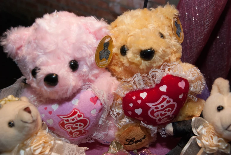 several stuffed teddy bears are sitting together, one with pink hair and the other has heart shaped hearts