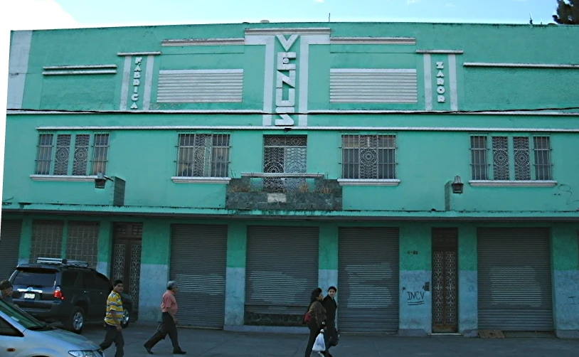 people walking down the street in front of a green building