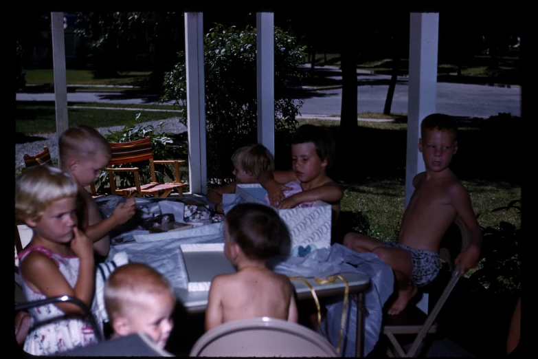 a group of children sitting at a table outside on patio furniture