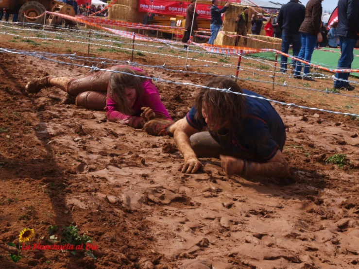 two people laying down in mud while others stand by