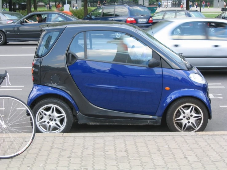 a blue small car sits on the curb next to a bicycle