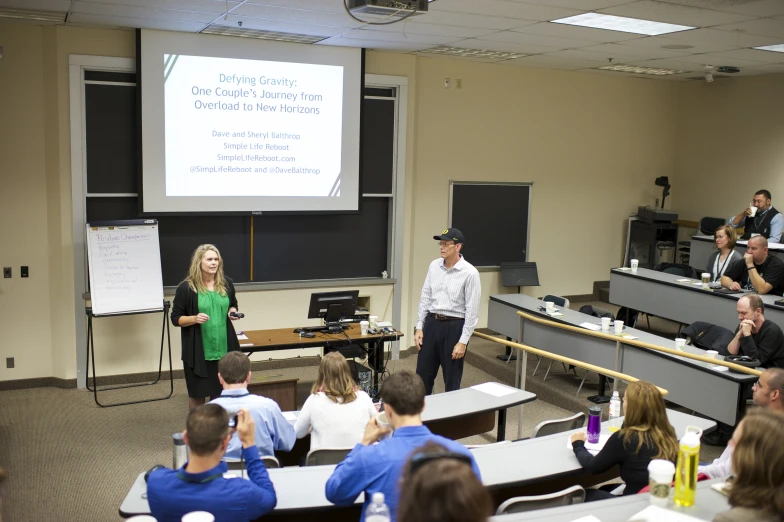 two people in front of a lecture room with a large screen