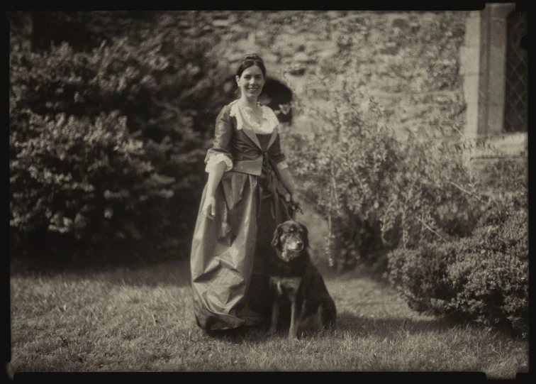 a lady with a dog on a lawn near shrubs