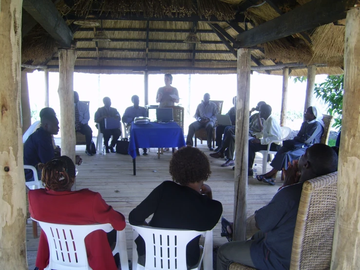 people sitting in chairs under umbrellas while others stand around