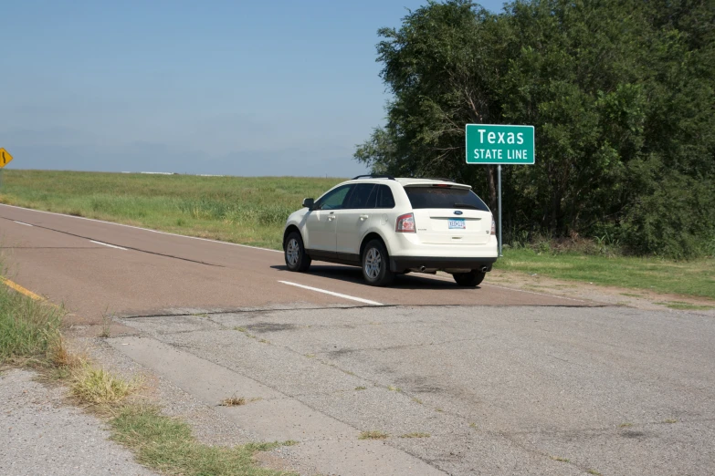 a white car is parked by the side of the road with a green street sign