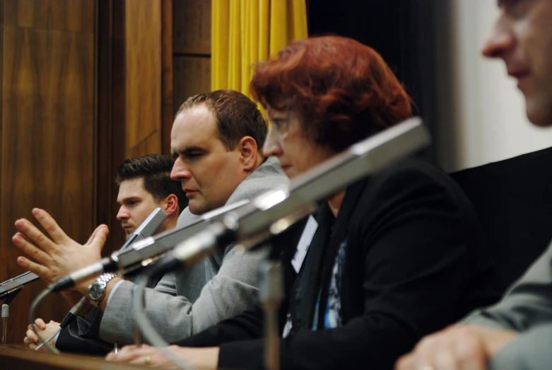 four people sit at a desk with microphones