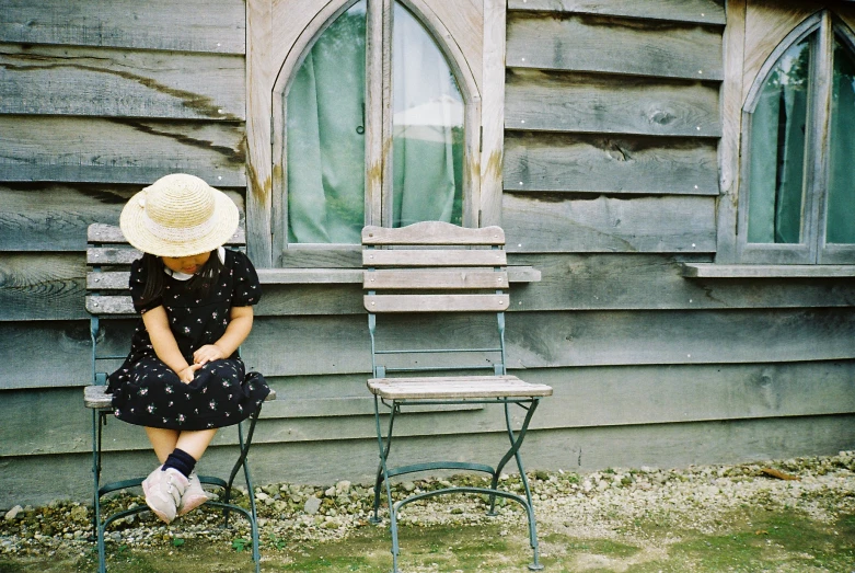 an old woman sitting in front of an old house with a hat on