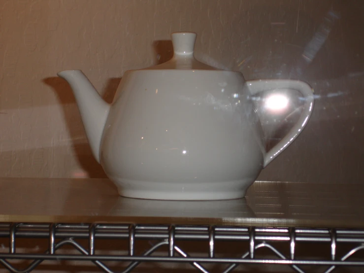 a white teapot sitting on top of a metal shelf