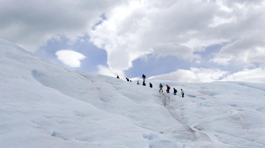 people walking up a snowy slope under a cloudy sky