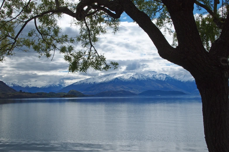 view of a lake, mountain range, and trees with snow on the top
