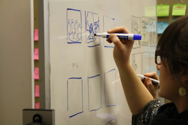 a woman writes on a whiteboard with blue markers