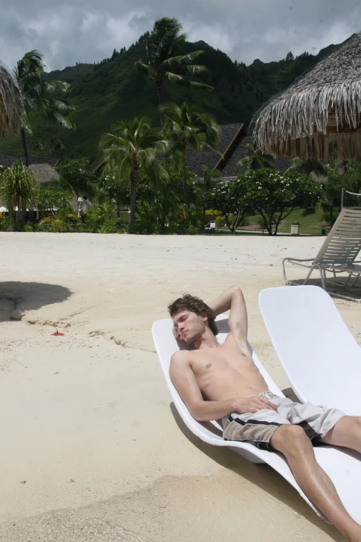 a man in swim trunks laying on a lounge chair at the beach