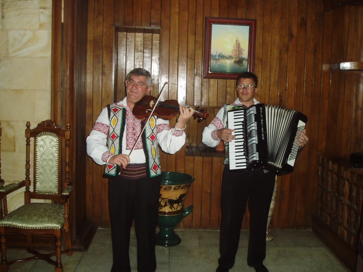 two men are standing in a room with a wooden wall