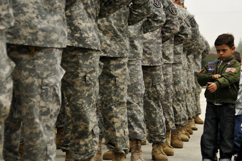 a little boy standing next to a lot of army pants