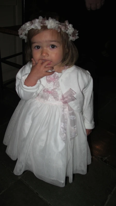 a girl wearing a white dress eating a piece of food