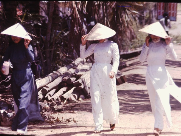 three women walk down the road in vietnamese hats