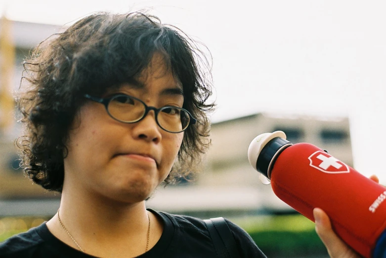 a person wearing glasses and holding a red bottle