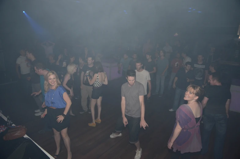 people in a dark club are dancing while a woman holds onto her phone