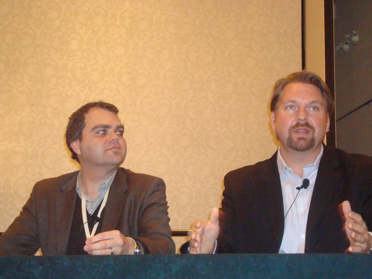 two men at a conference, one with a cell phone